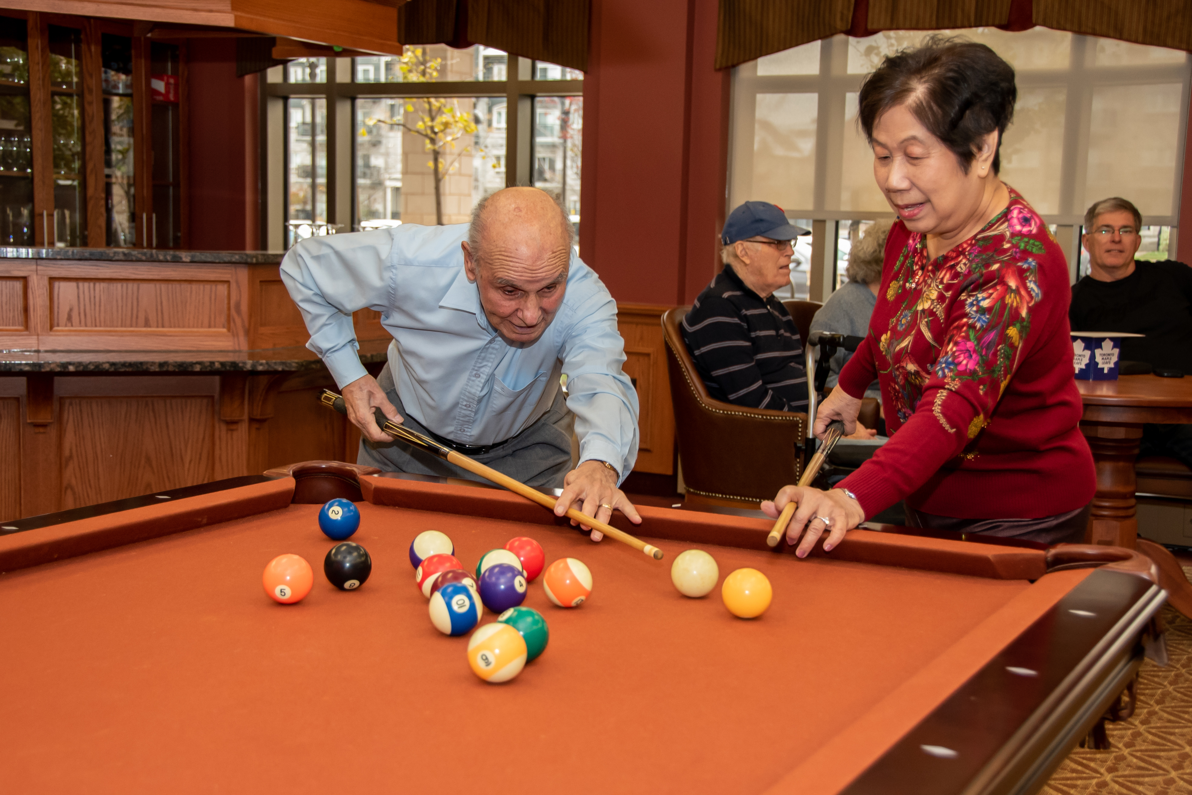Diverse seniors share in a game of billiards in the Village social club