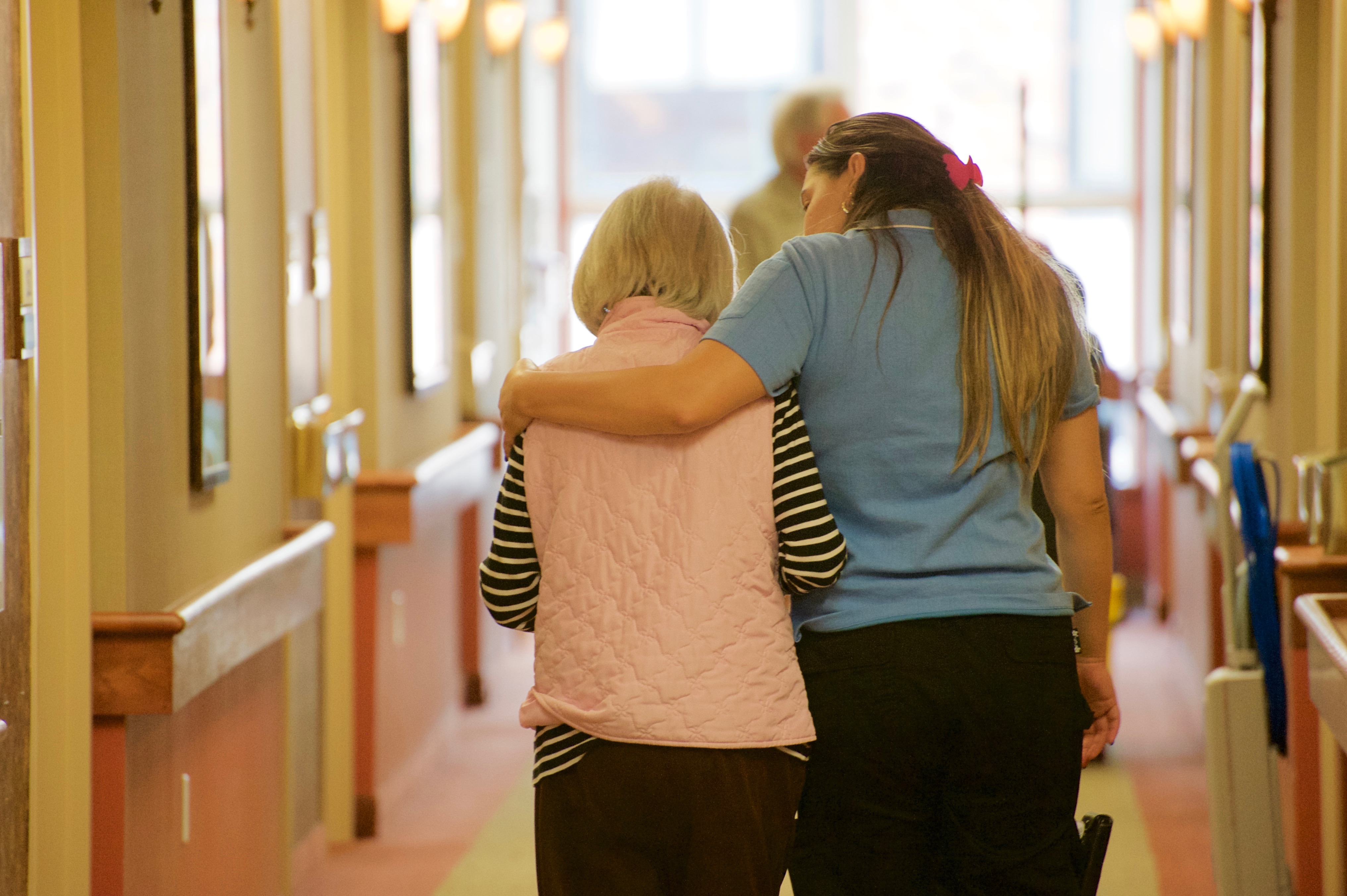Schlegel Villages team member walks in hallway hugging resident