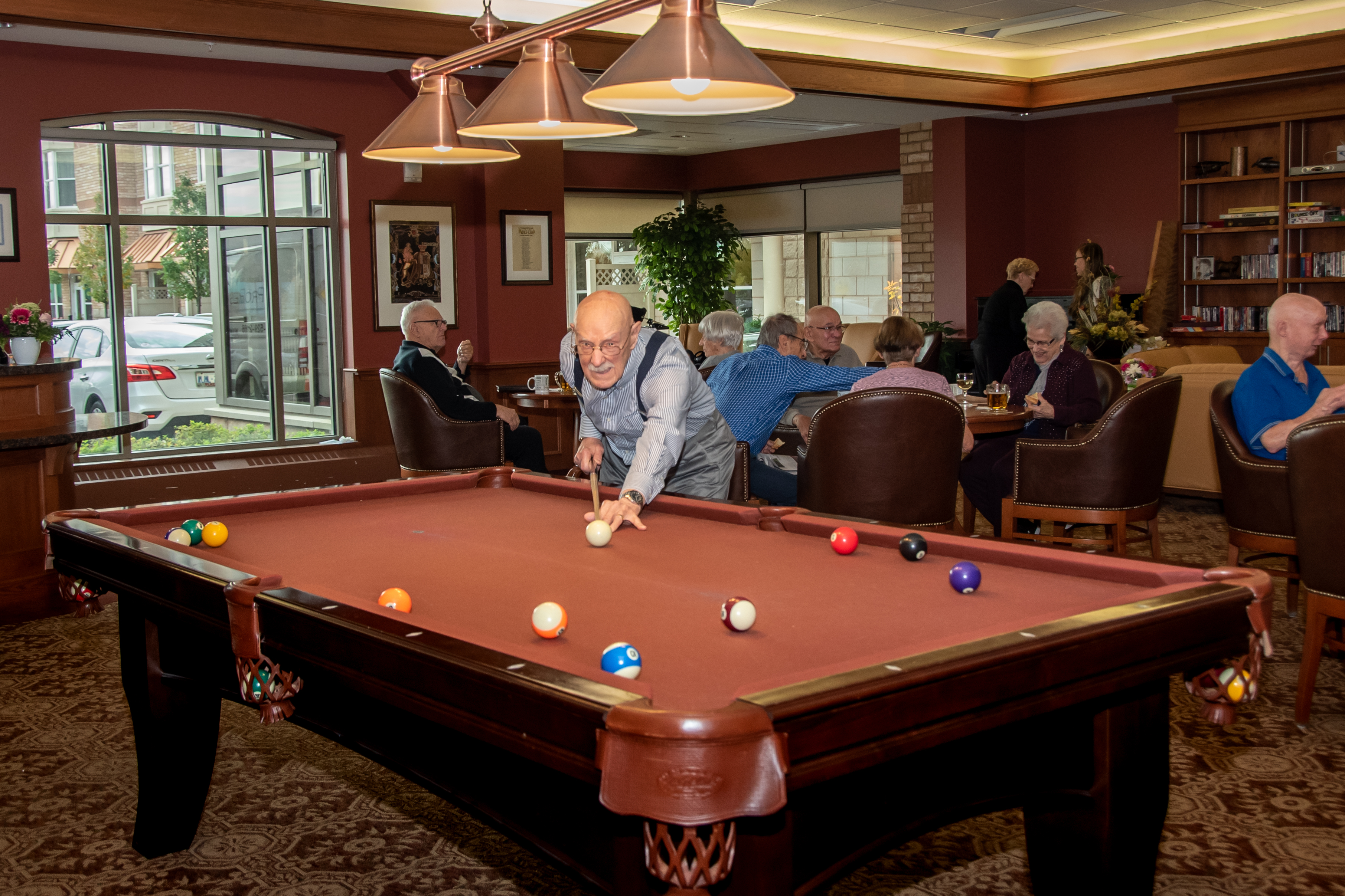 Male resident playing pool in the Social Club while other residents socialize.