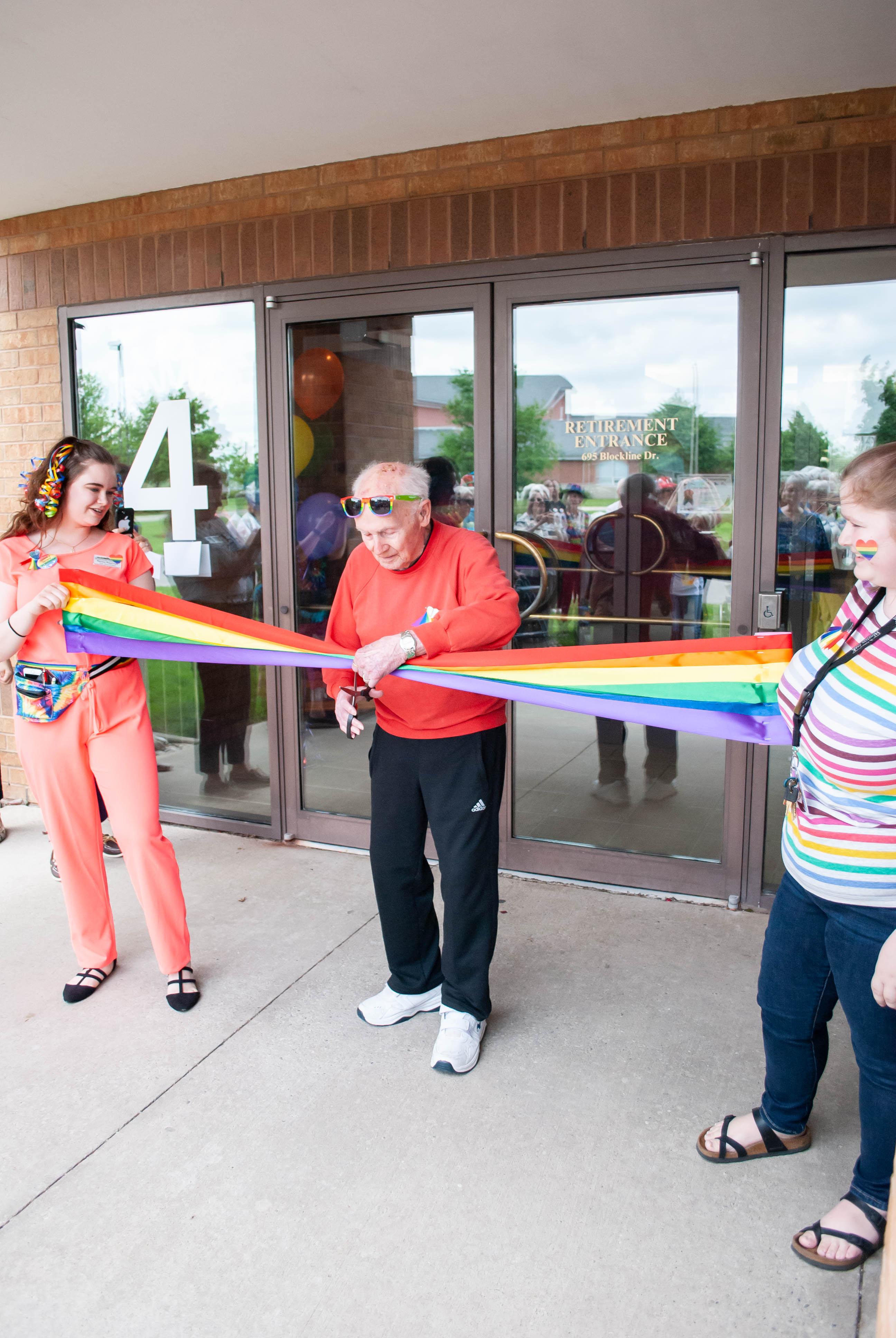 Resident cutting a Pride ribbon with two team members