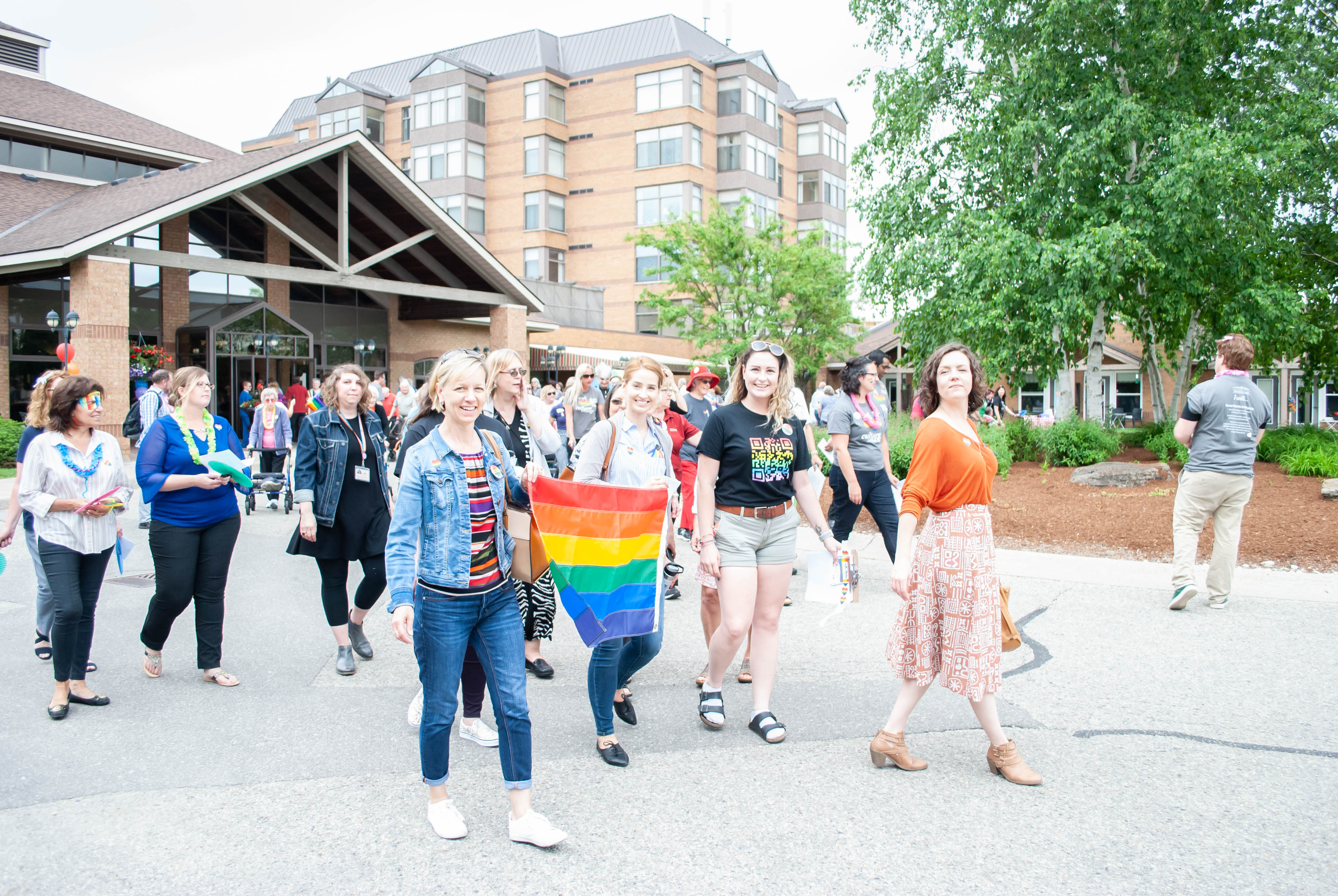 team members, residents and visitors walk outside winston park carrying a pride flag