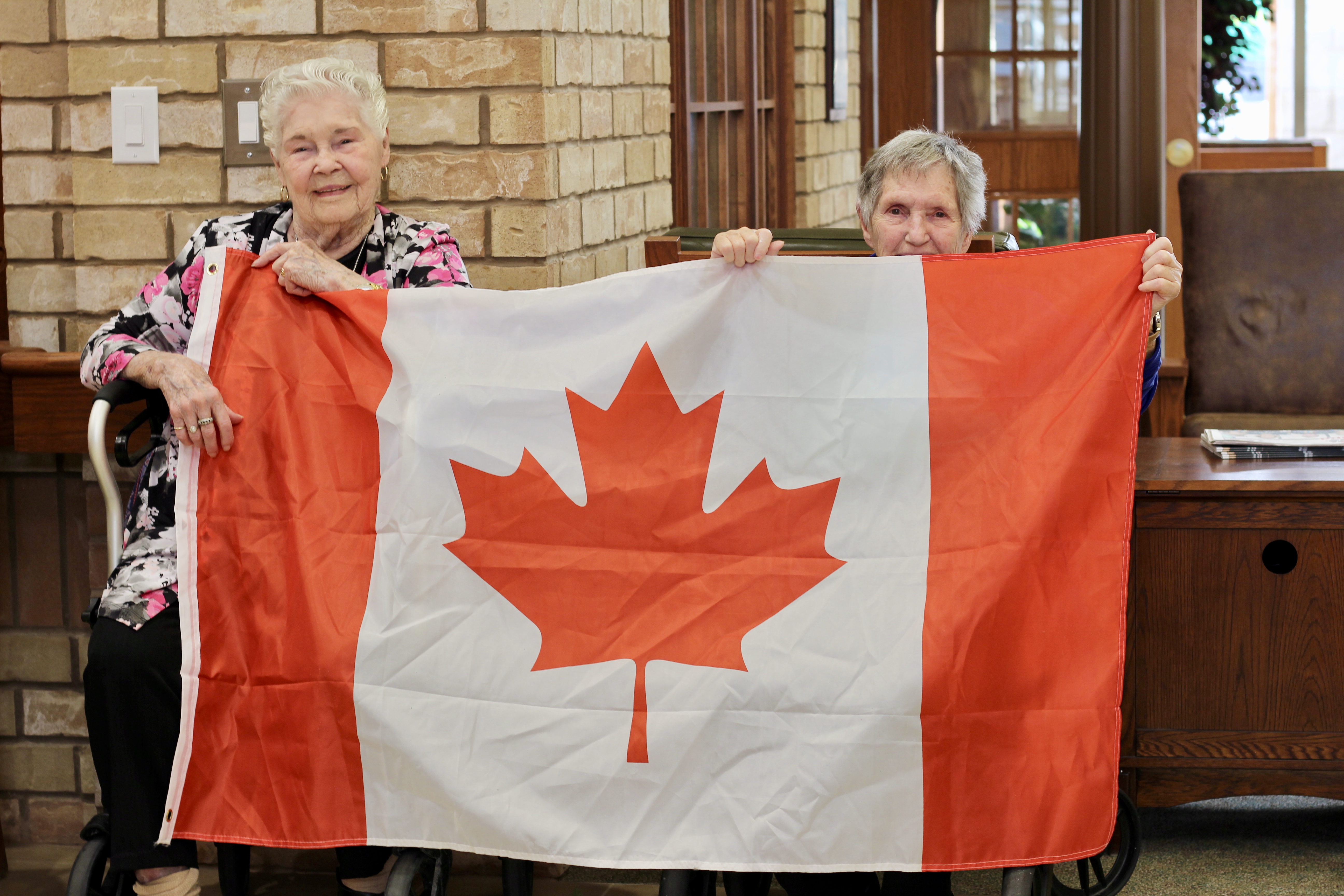 Two ladies holding up the Canada Flag at the Village - We are a proud Canadian Organization