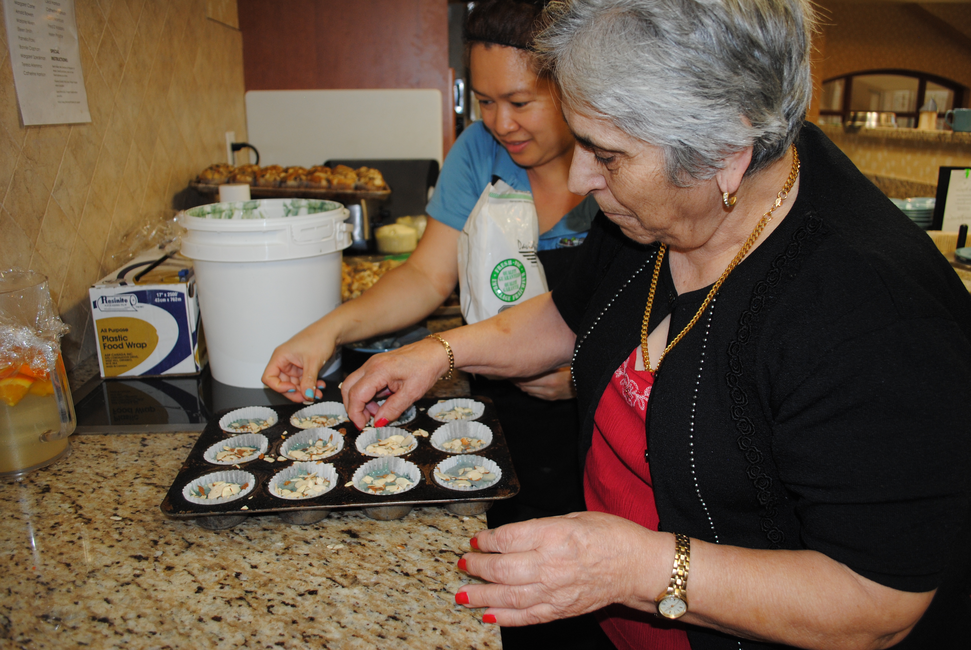 Resident helping a team member making muffins in the open serverie