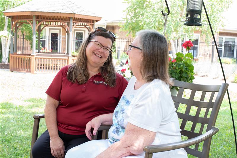 Team member and resident engage in laughter outside on a bench