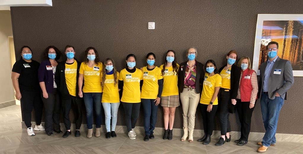 Support office team members stand against a wall with innovation catalysts wearing yellow shirts. 