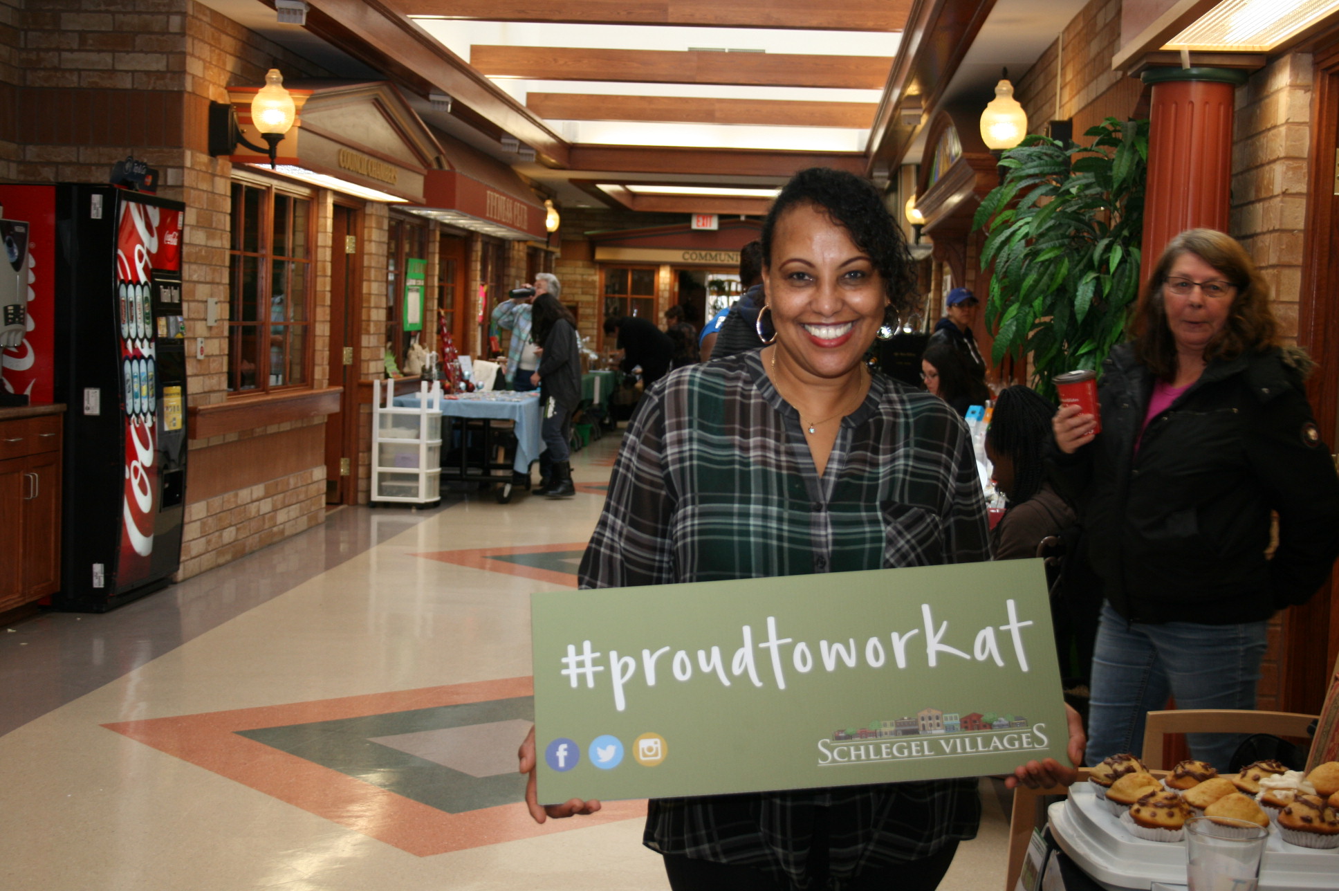 Team member smiling with the #ProudToWorkAt sign on Main Street