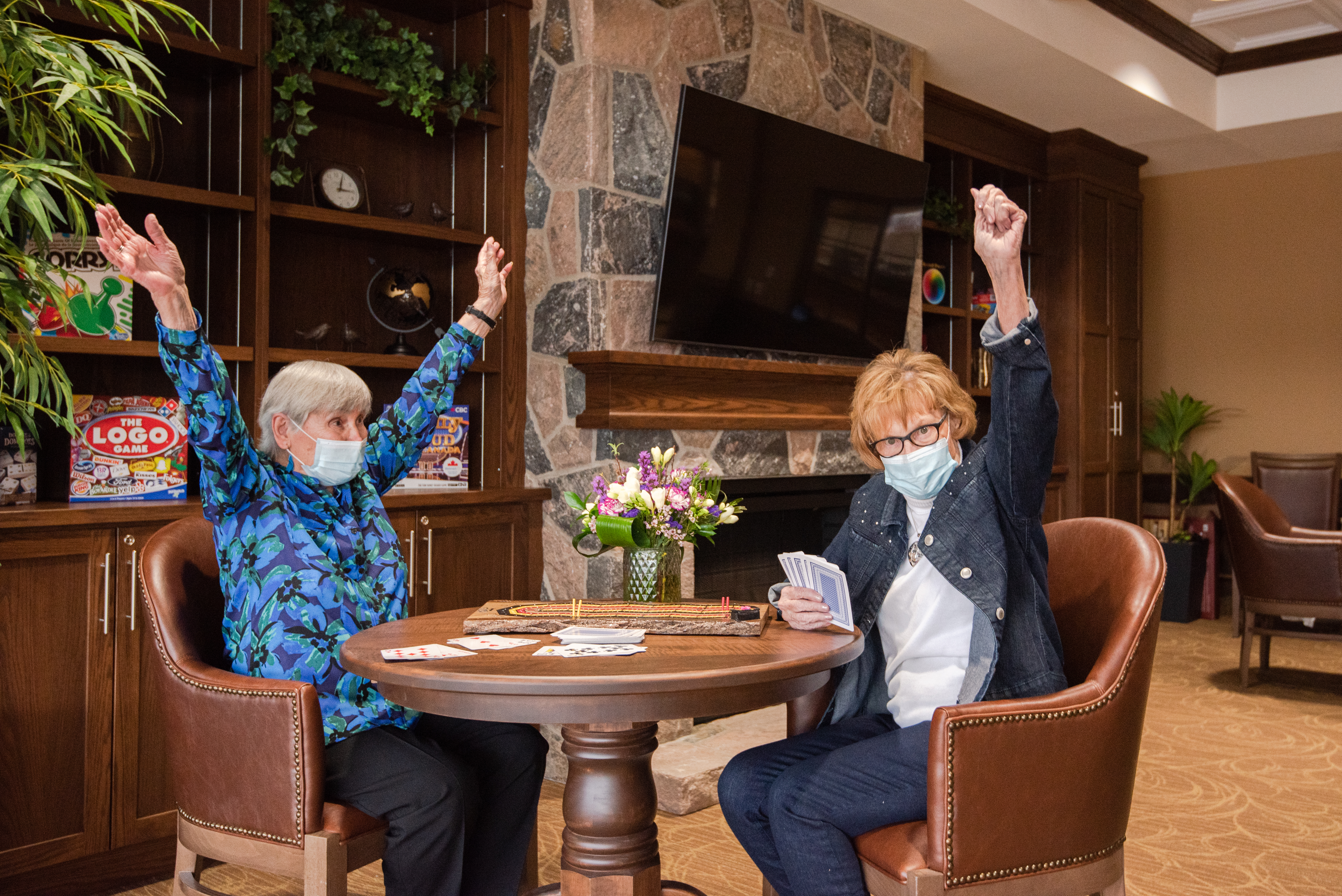 Two residents playing cards in the Social Club, hands raised in victory