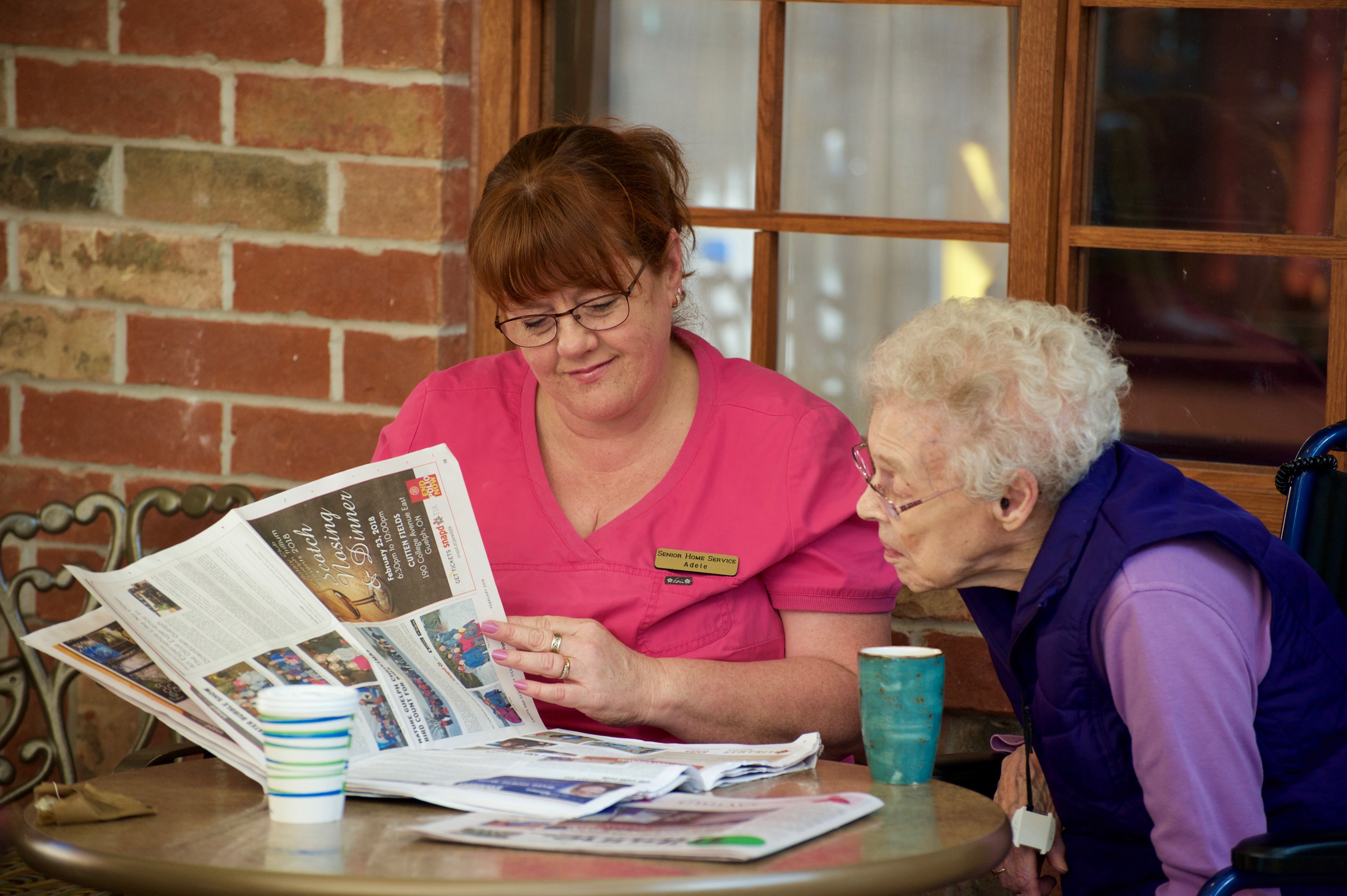 Resident and caregiver reading the newspaper over a coffee