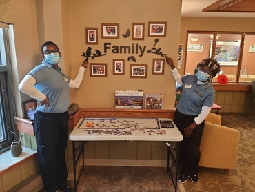 Grace and Joy stand at a wall adorned with photos and the word family.&nbsp;