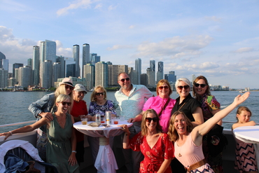 A large group gathers together upon the boat with the Toronto skyline in the distance.