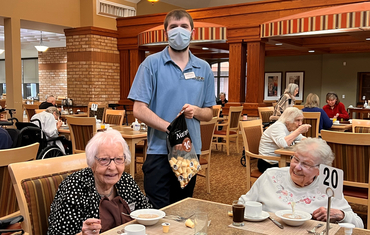 Jordan stands between two ladies laughing as her serves them breakfast. 
