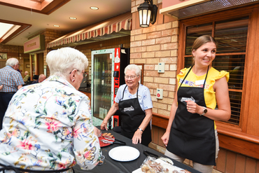 Meaningful engagement between residents and team members is always a focus in the Villages, as seen here with residents and team members conversing over a table of baked good during the Pursuit of Passions event at University Gates. 
