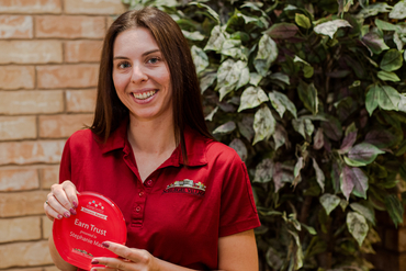 Stephanie stands with a broad smile, displaying the success award she received for "earning trust."