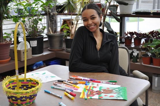 Adriana poses behind a desk with a broad smile upon her face. 