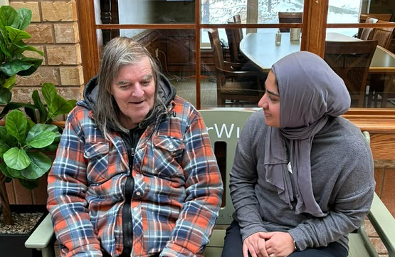 Nurse Practitioner Amera sits with a resident upon the green ElderWisdom bench. 
