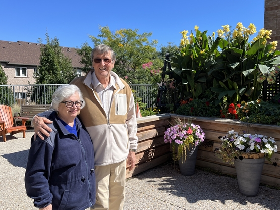 Armando and Mirella stand together alongside the gardens in the courtyard at Erin Meadows.
