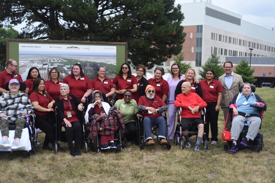Team members and residents from Hamilton Continuing Care gather in front of the rendering of their new home to be, the Village of Fennell Ridge. 
