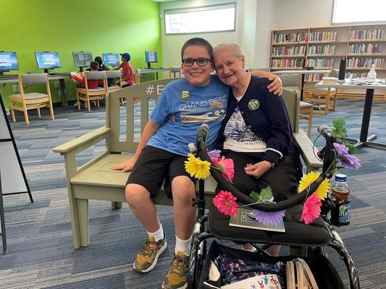 A young person embraces an older person while sitting upon the Green Bench at the Essex County Library.