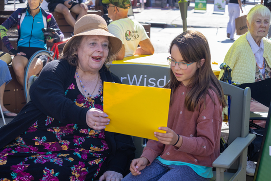 Kaye sits upon the Green Bench with a young lady named Penny, looking at a homemade card. 
