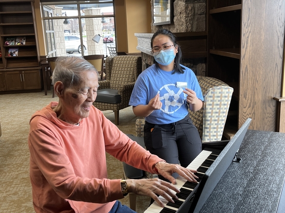 Eusebio plays piano and sings while Irah Jane sits alongside and listens. 