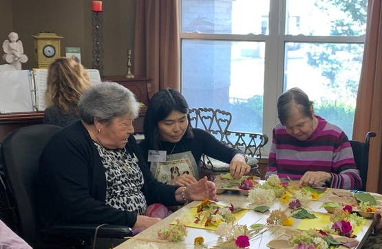 Flo is at a table alongside two residents helping them express themselves through art. 
