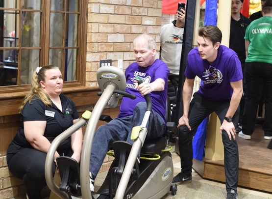 Harry competes upon the Nu-Step Machine at the Schlegel Olympics as he is encouraged by two team members. 