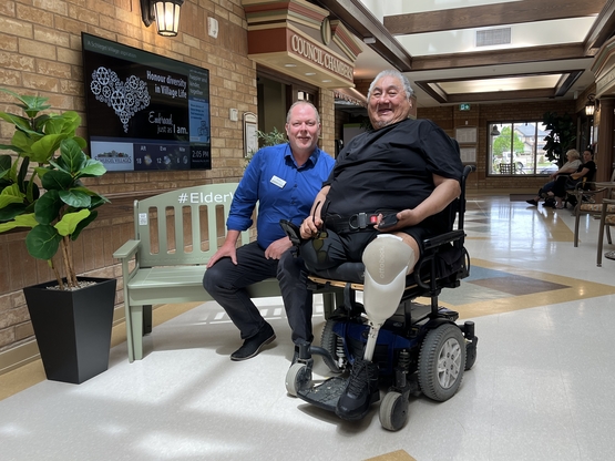 Gerald and Village Voice writer Kristian Partington sit alongside the Elderwisdom Green Bench in the Village of Ridgeview Court.