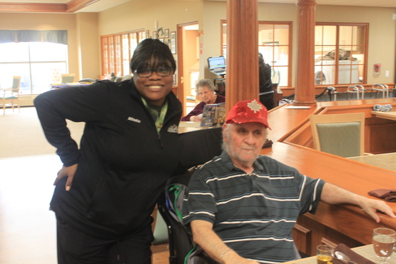 Attasha poses with a wide smile beside a gentleman in the dining room in one of the Erin Meadows retirement neighbourhoods. 
