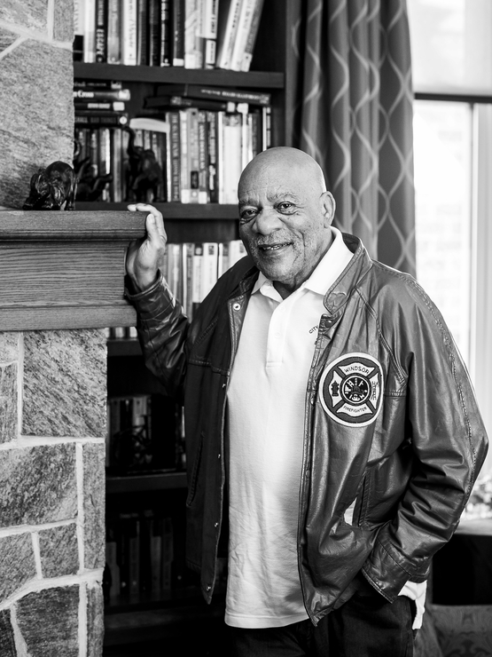 Ron Jones black and white portrait with books in the background and wearing his Windsor Fire jacket