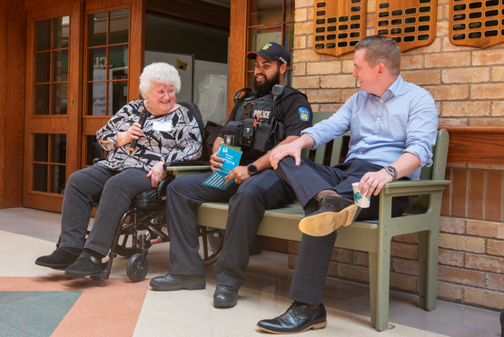 Donna sits with a police officer and politician sharing wisdom upon the Green Bench.