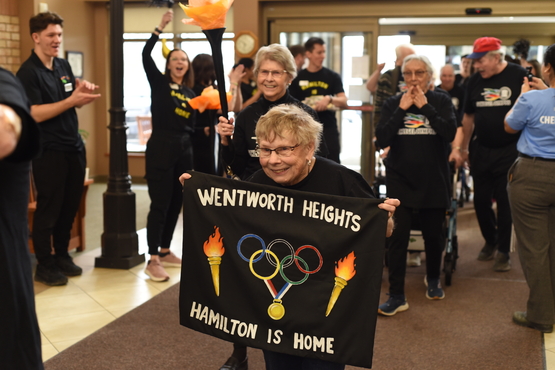 A resident from Wentworth Heights leads her team into the Village with a sign that says "Hamilton is Home."