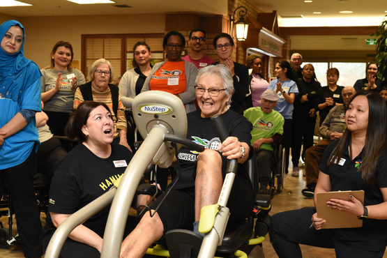 Team members from all parts of the Village have a part to play in supporting residents, as we see here with different team members cheering a resident working out on a Nu-Step Machine. 