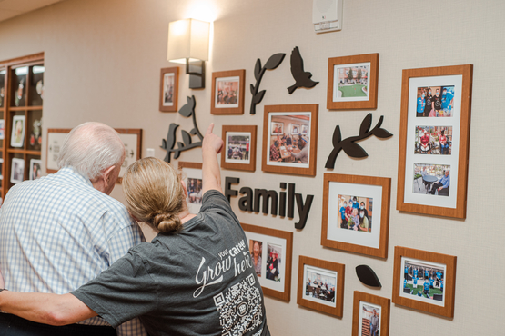 A team member and resident look upon a wall adorned with the word "family" and photos to inspire conversation. This is a key thoughtful design element of the Enhanced Supportive Neighbourhood at Ridgeview Court.