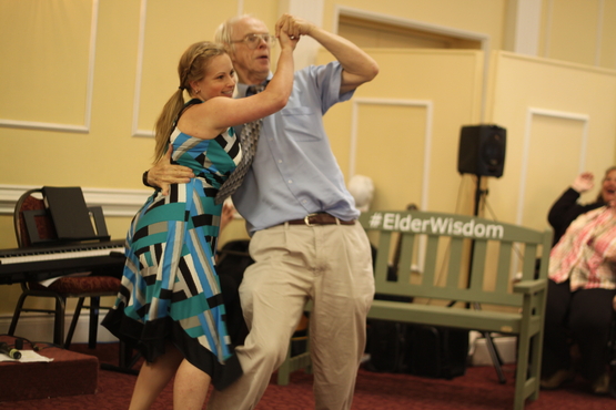 Phil and Tiffany dance together with the #ElderWisdom Green Bench in the background. 