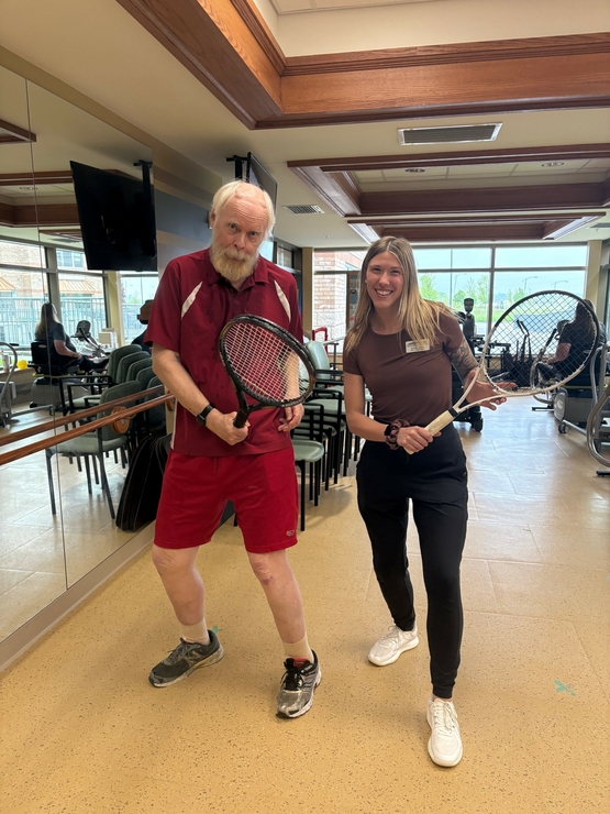 Sarah and Phil pose together in the University Gates fitness centre with their tennis racquets poised.