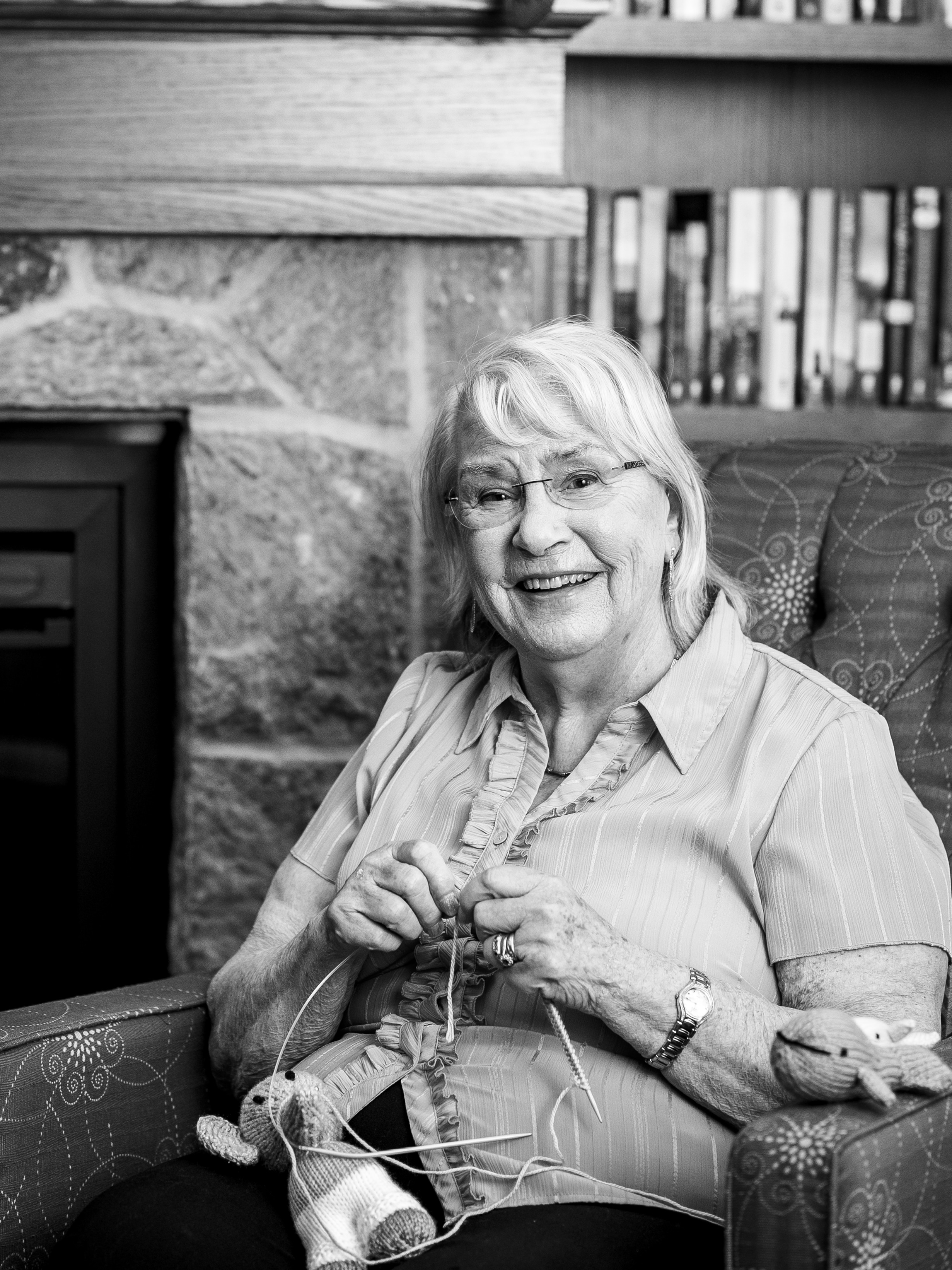Jill Barrett knitting in the library at the Village in a black and white portrait