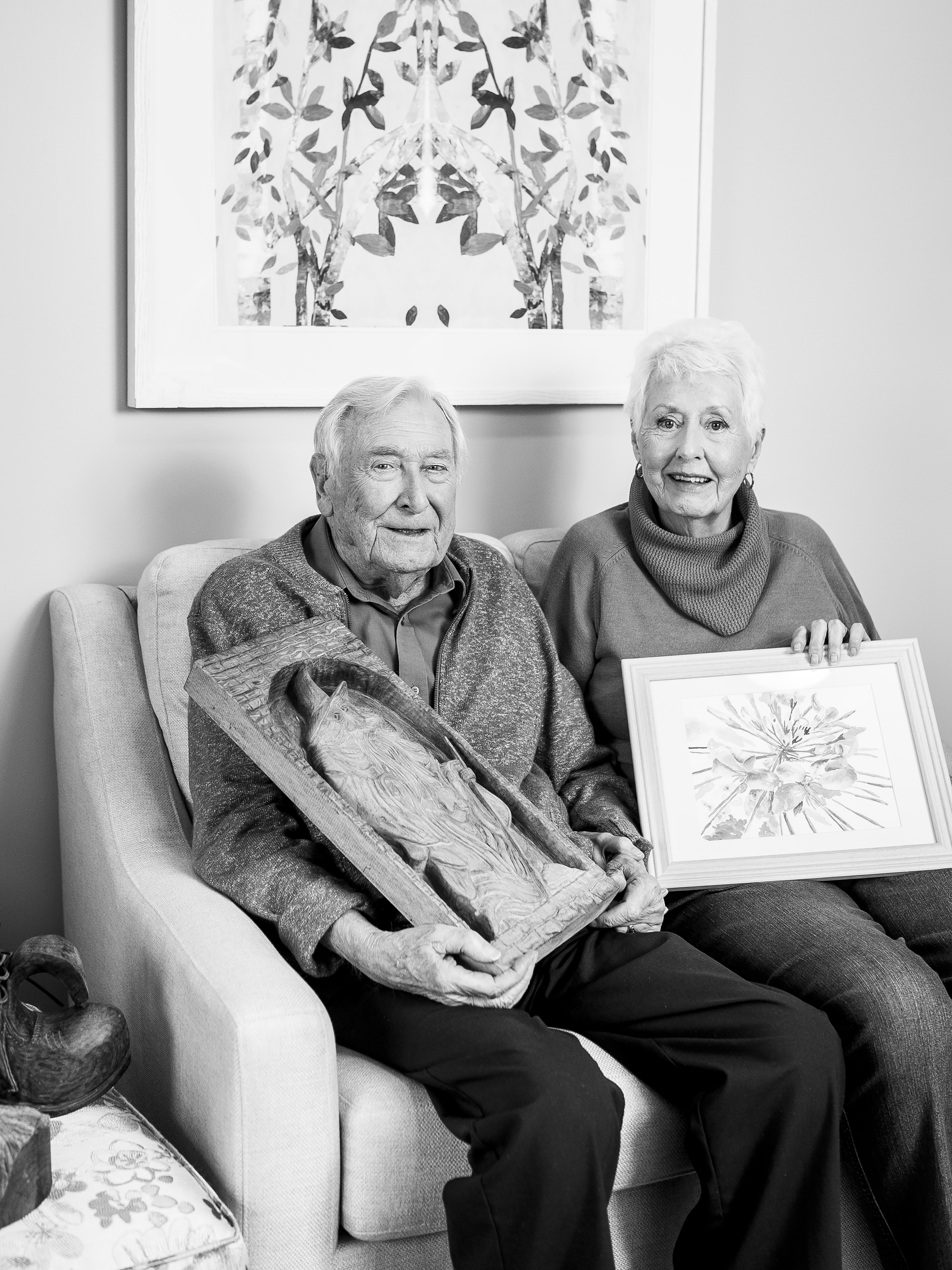 John holding a wood carving and Doris holding a painting in a black and white portrait