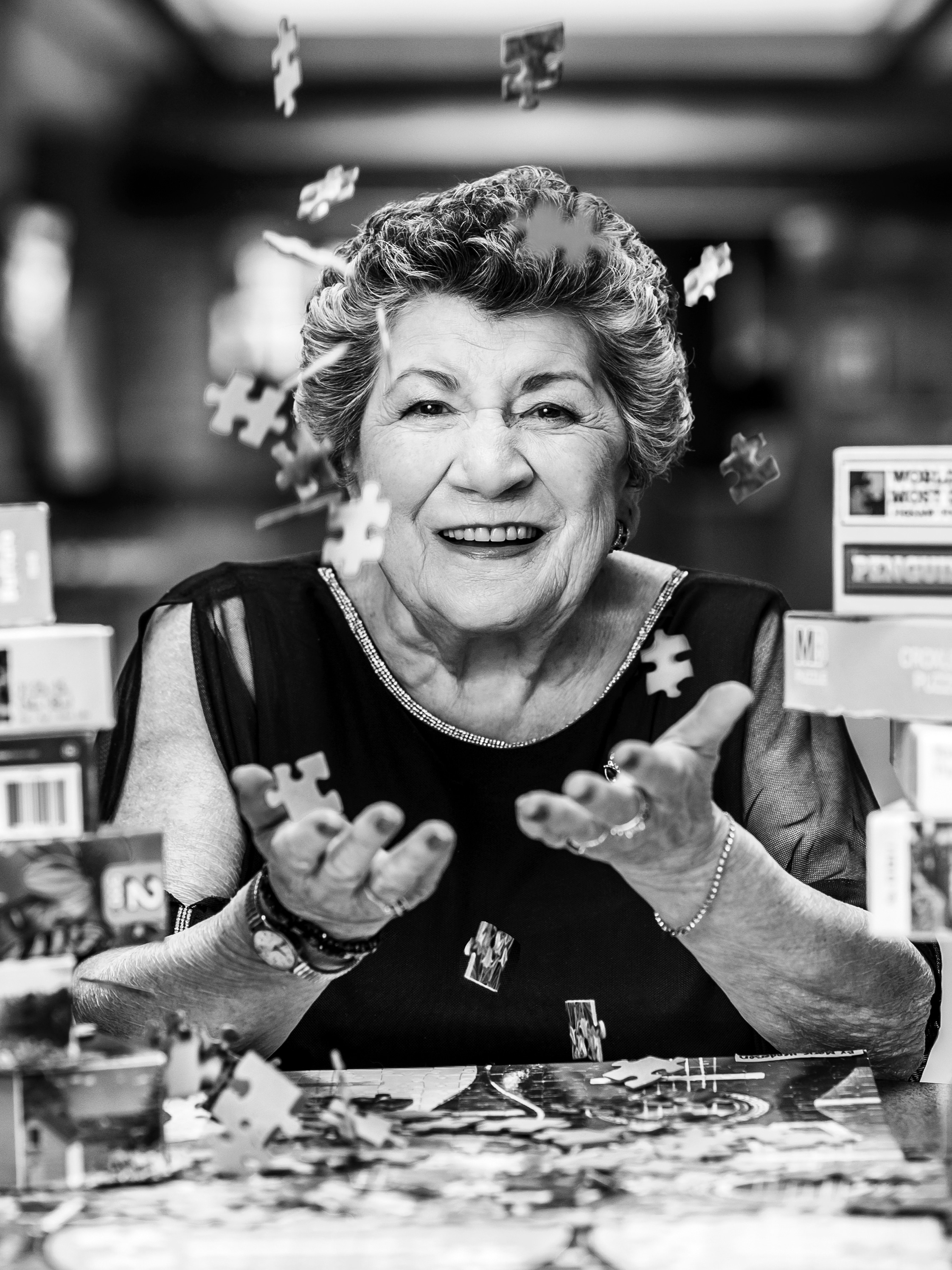 Marie Henderson black and white portrait sitting at a table of puzzles and puzzle pieces falling into her hands