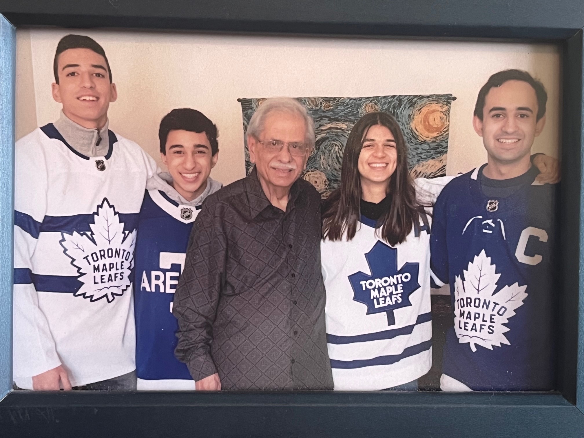 Nari stands with his grandchildren, who are wearing hockey jerseys and smiling bright. 