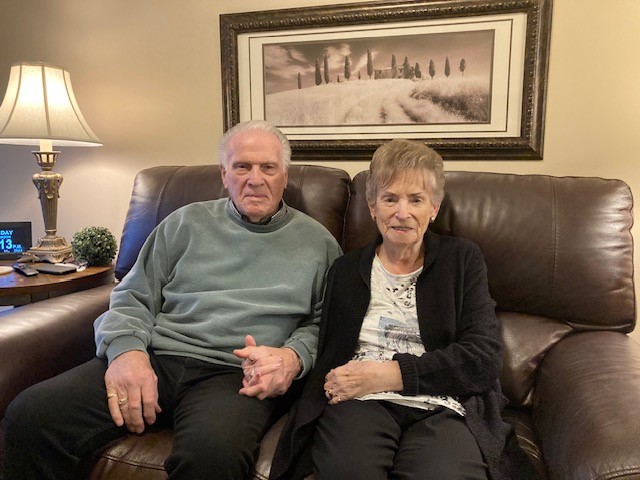 Bruce and Dorothy sit holding hands on their sofa in their suite at Glendale Crossing. 