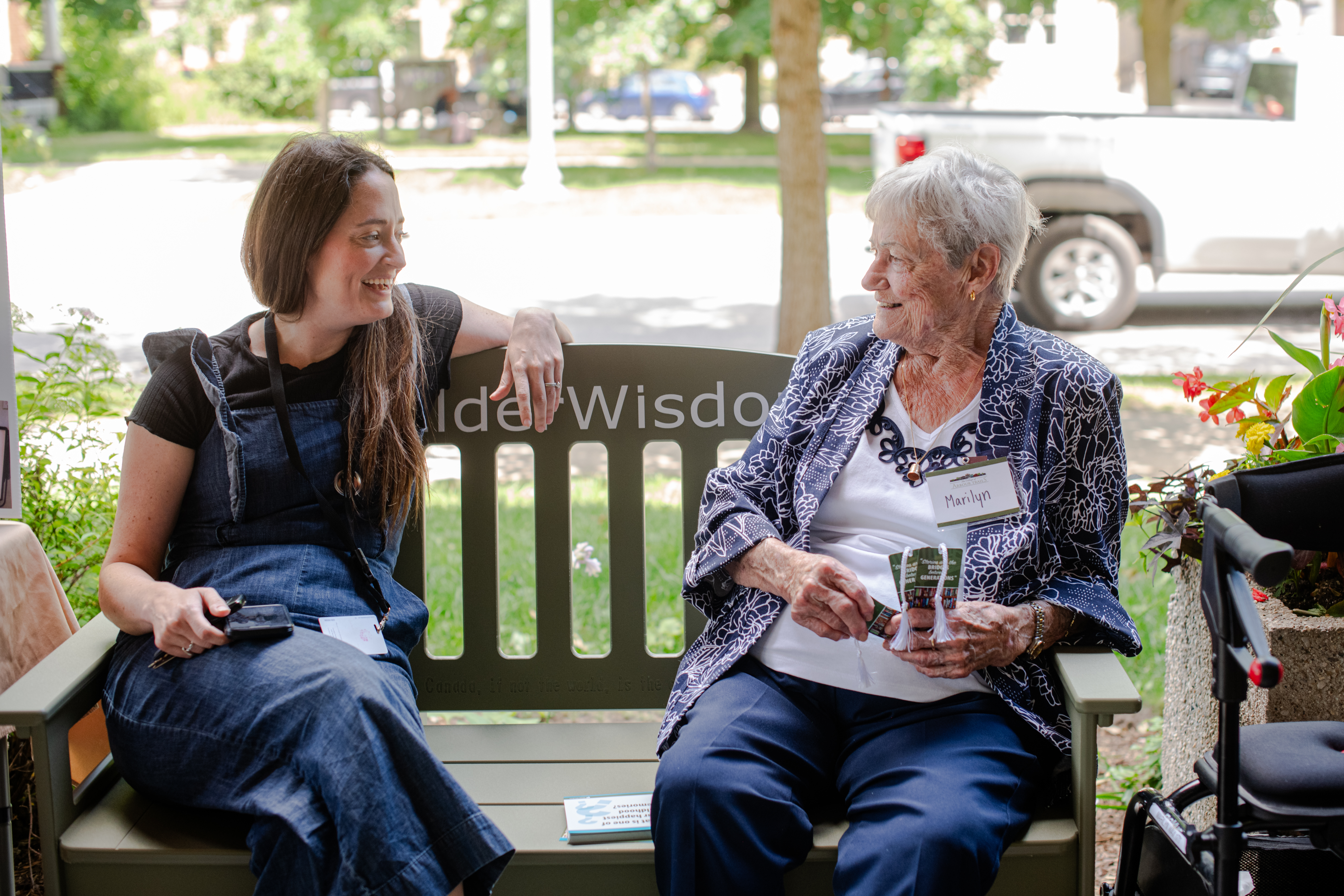 Arbour Trails resident Marilyn Wax shares a conversation with a younger person while sitting on the Elder Wisdom Green Bench. 