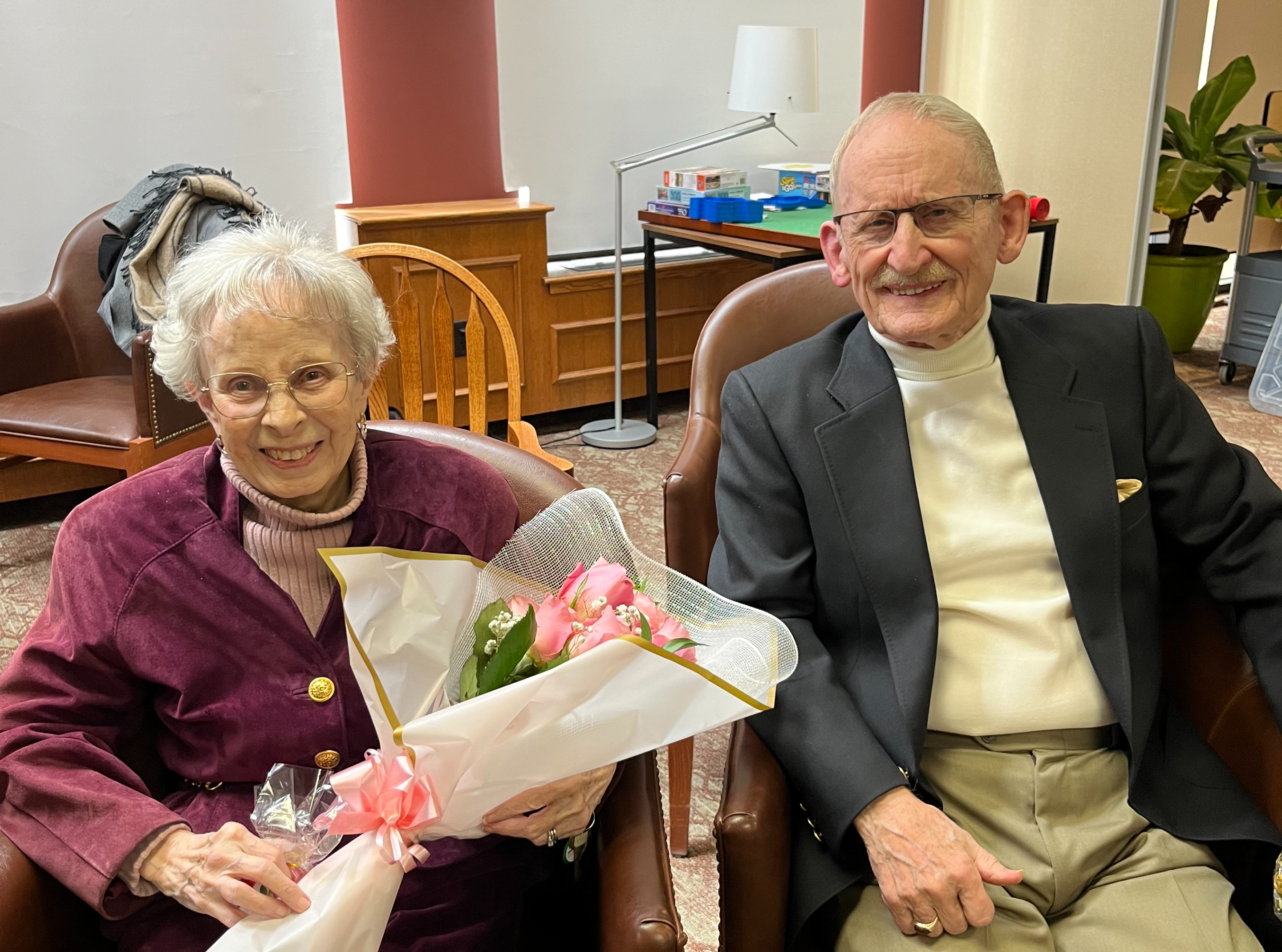 Alexander and Joan smile as they sit beside each other before their vow renewal, a beautiful bouquet of flowers nestled in Joan's arms. 