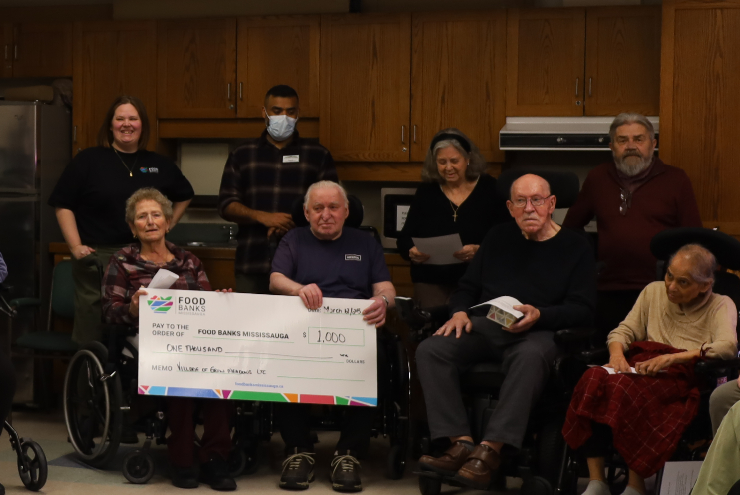 Erin Meadows residents gather with Stacey Kelly from Food Banks Mississauga with a large cheque for a $1,000 donation.