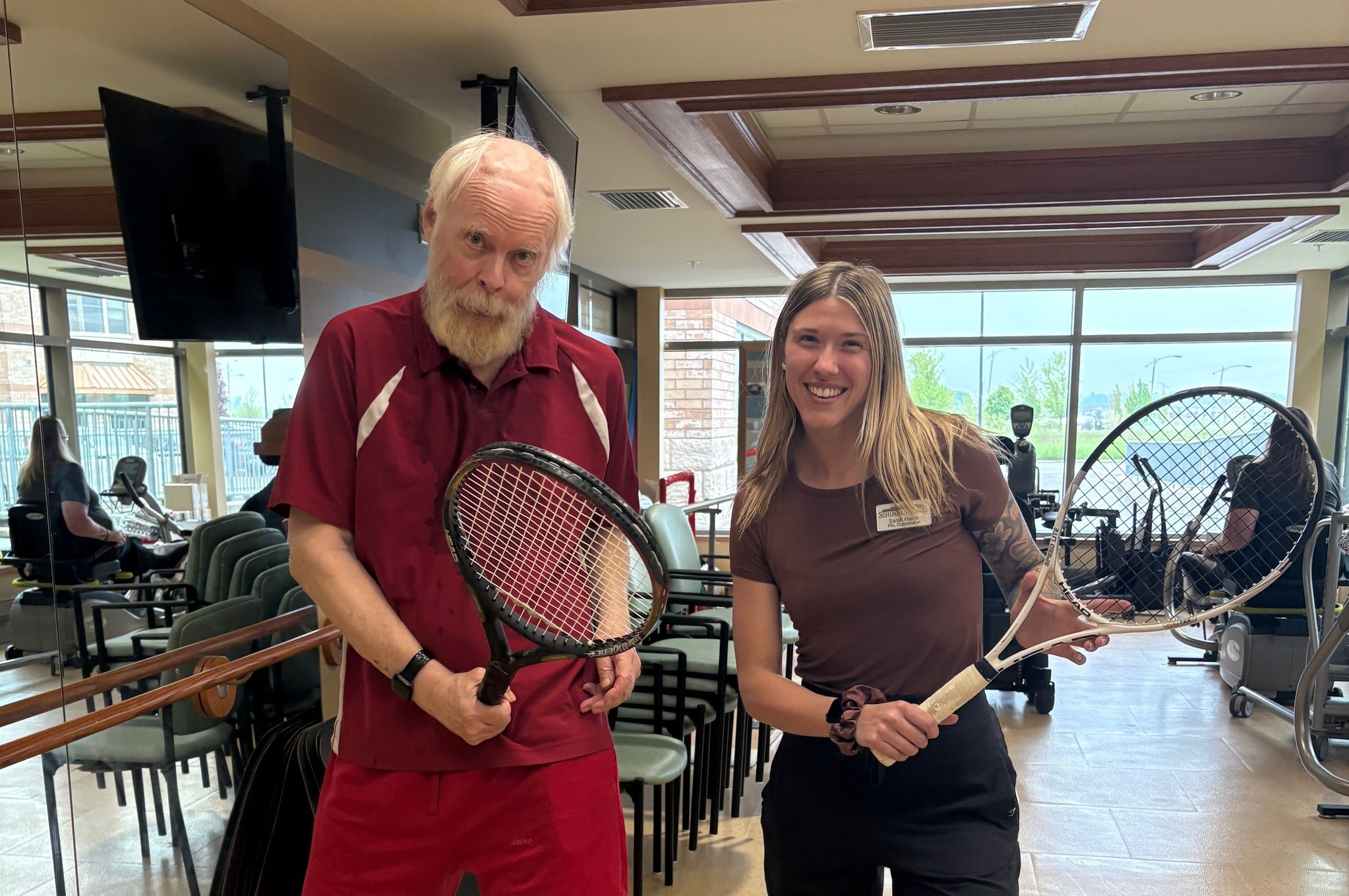 Sarah and Phil pose together in the University Gates fitness centre with their tennis racquets poised.