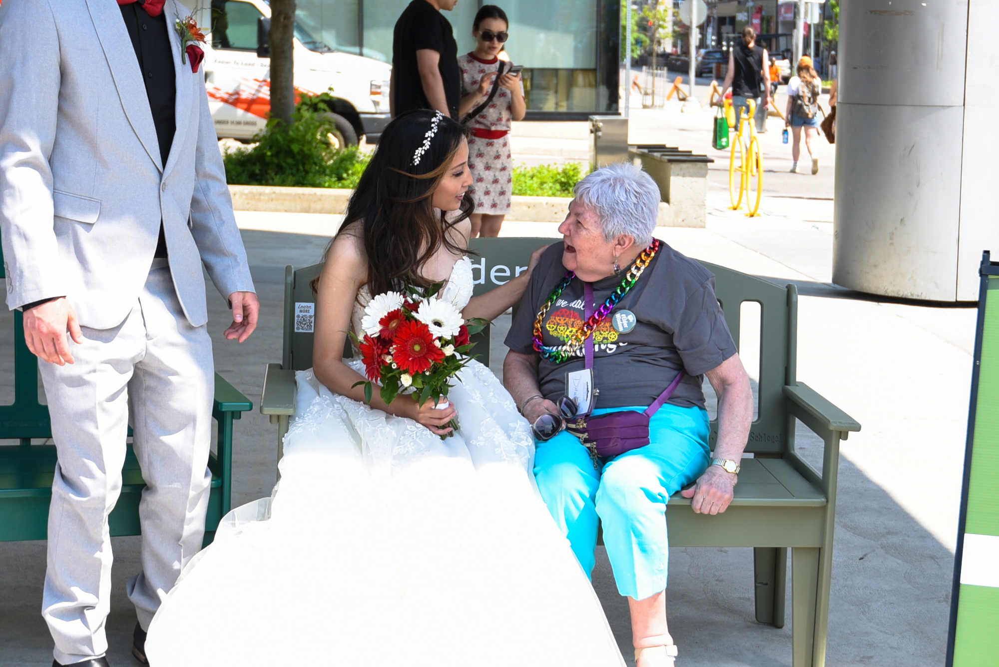 A bride in her wedding dress sits upon the Green Bench alongside a Schlegel Villages resident.