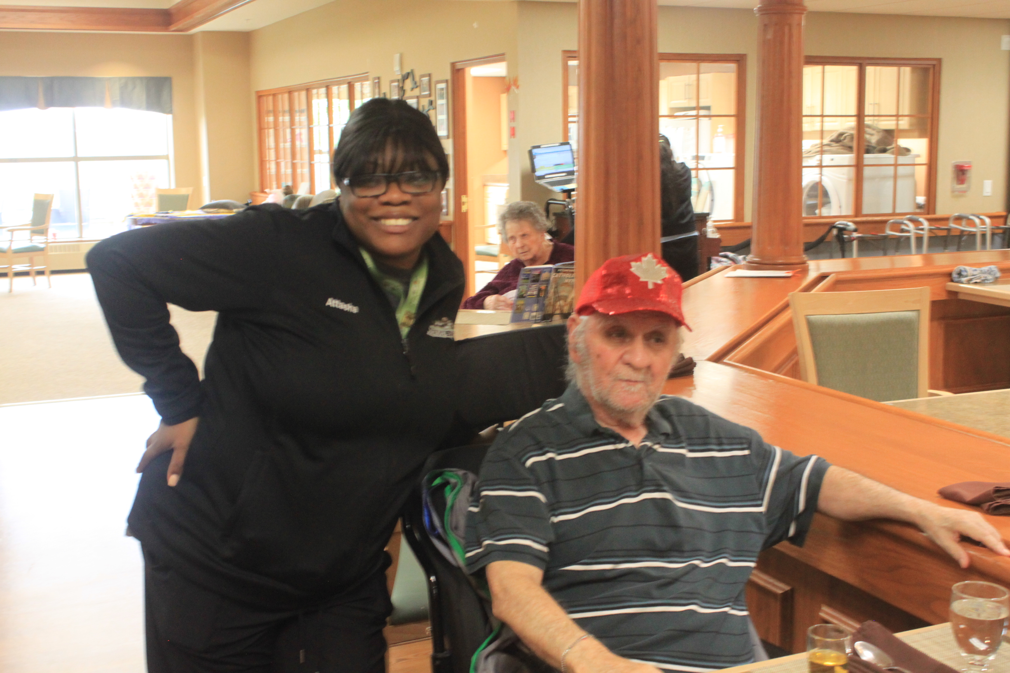 Attasha poses with a wide smile beside a gentleman in the dining room in one of the Erin Meadows retirement neighbourhoods. 