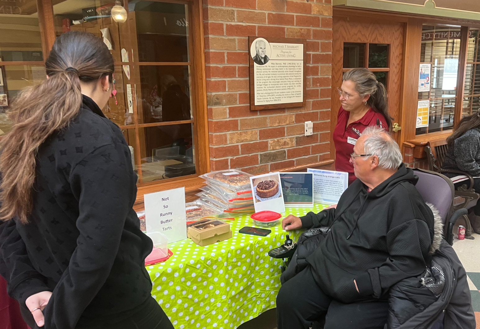 Wayne speaks with team members who've stopped by his table of baked goods during the Wednesday market at The Village of St. Clair. 