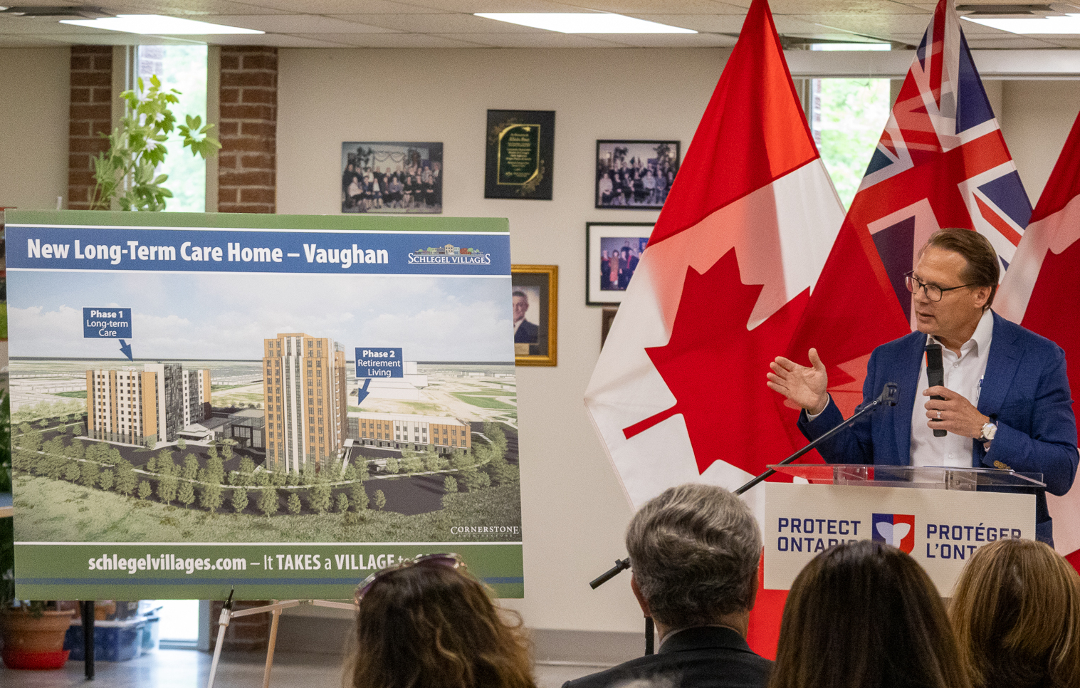 During an announcement July 28, Jamie Schlegel stands alongside a rendering of the new Village to be built in Vaughan, Ontario. 