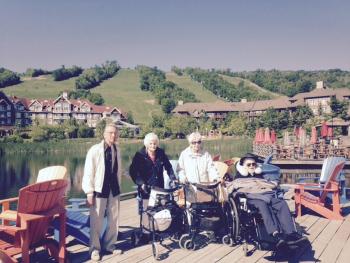 Residents Roy, Shirley, Nancy, and Jack taking a group photo in front of a lake, with the Collingwood hills and resort behind them