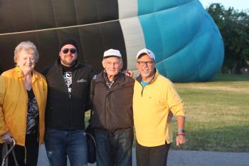 Four people stand in front of a hot air balloon being inflated behind them
